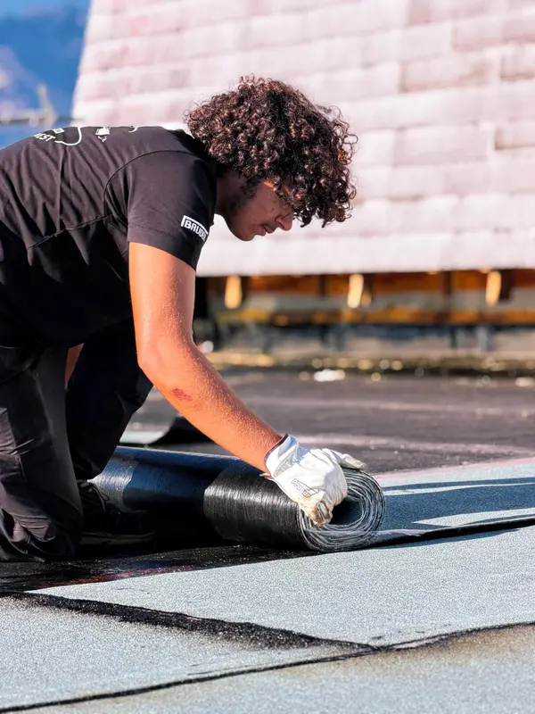 Ouvrier STRED Swiss déroulant un rouleau de bitume en toiture